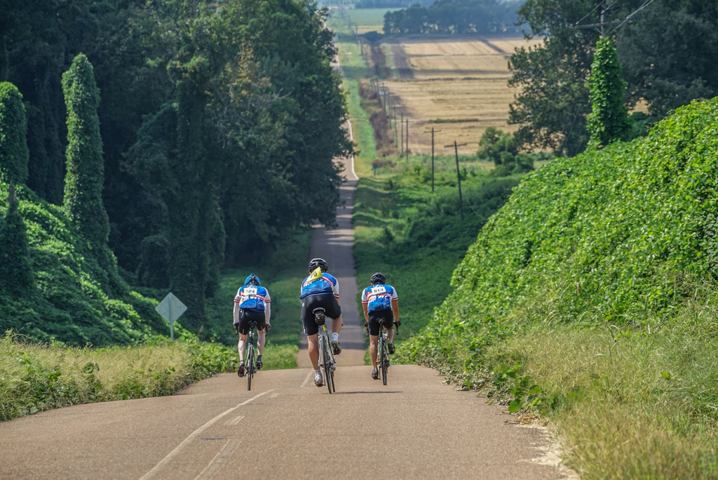 Three cyclists rinding down a long hill 