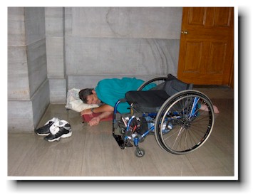 Man sleeps on the floor beside his wheelchair.