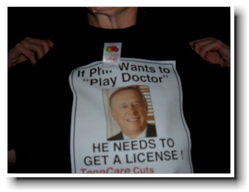 Activist holds up a t-shirt: If Phil Wants to "Play Doctor" - HE NEEDS TO GET A LICENSE!